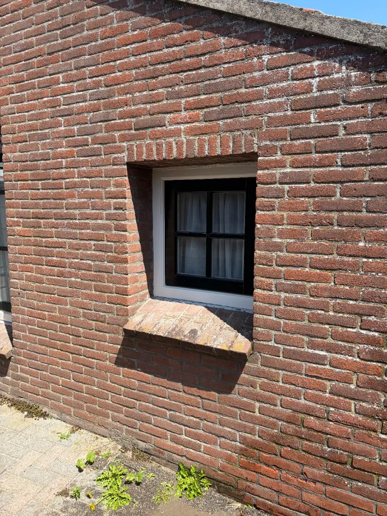 Bakstenen gevel rond raam voor reiniging, met vuil en aanslag op steen en voeg