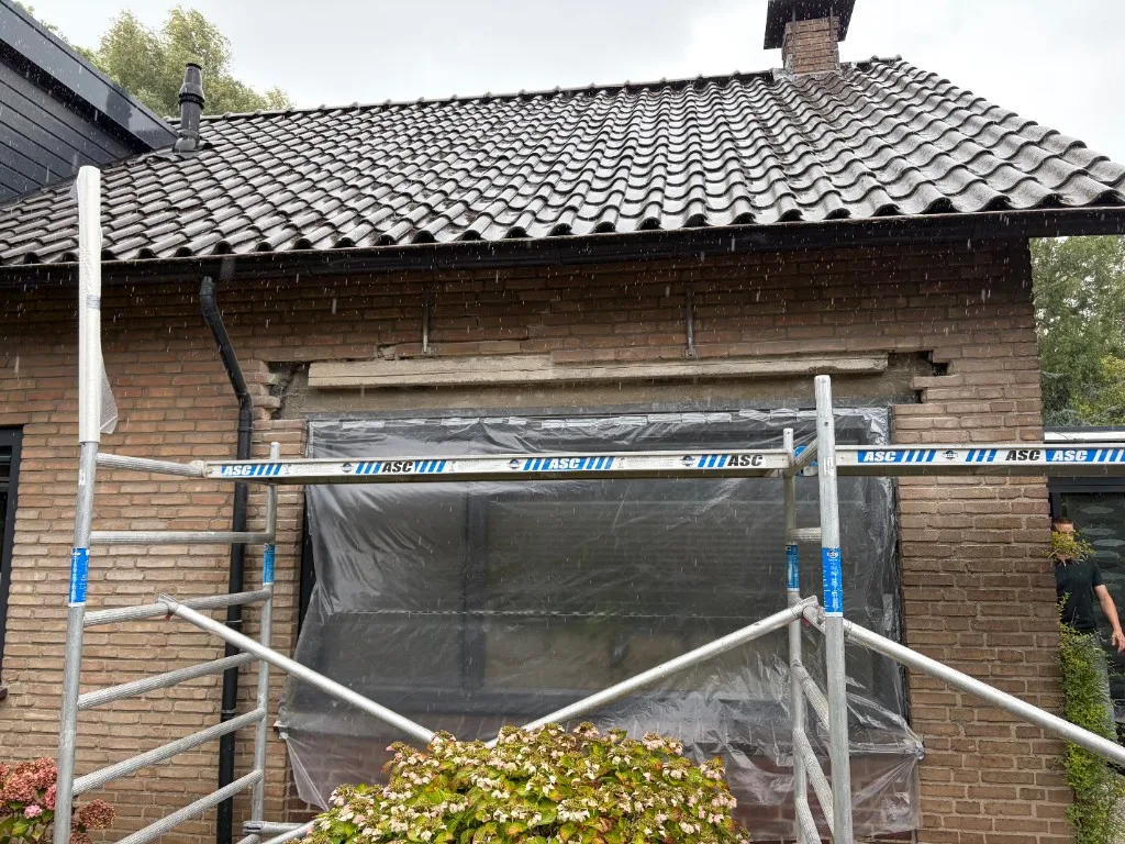 Metselwerk boven kozijn uitgehakt — kozijn beschermd met folie, geveldragers ter ondersteuning