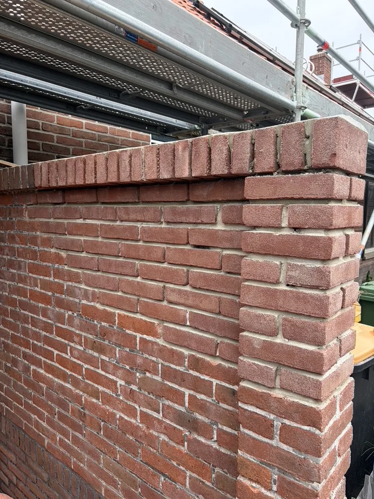 Detail hoek tuinmuur Brouwershaven: rollaag met aangesmeerd betonnen dakje en strak platvol voegwerk