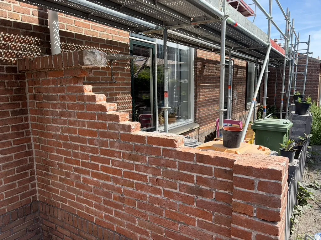 Tuinmuur Brouwershaven tijdens het opnieuw opmetselen, met steiger en trappende steenlagen