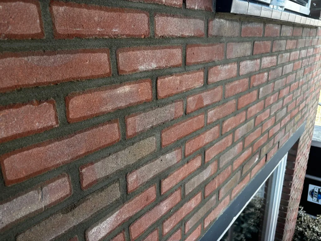 Rode bakstenen wand met platvol voegwerk in een donkere morteltint